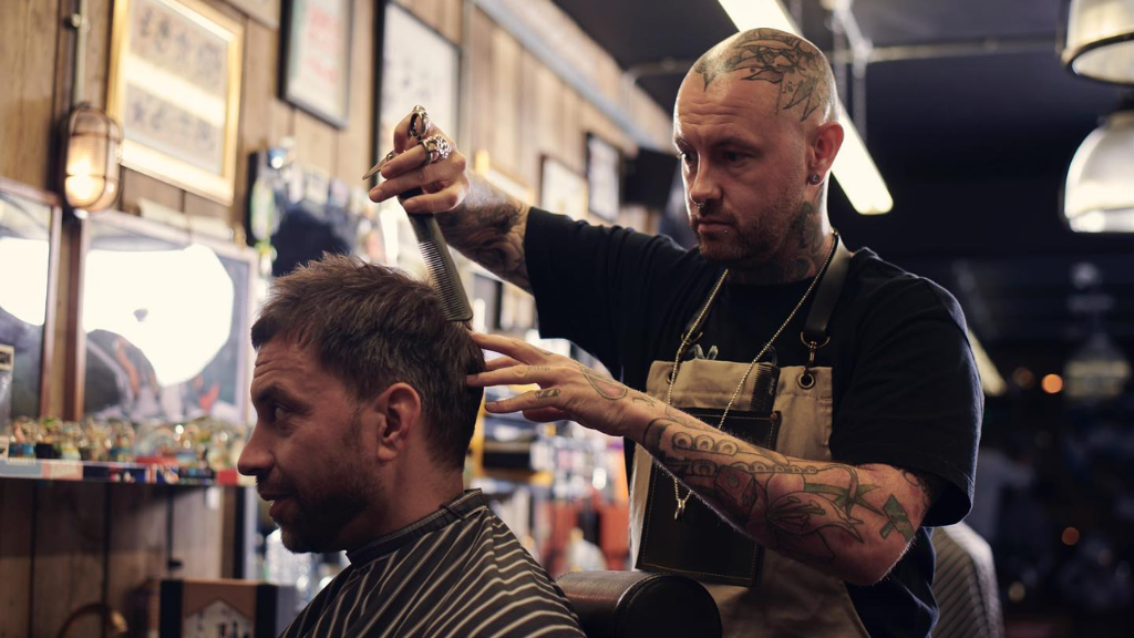 A tattooed barber cutting hair with comb in hand.